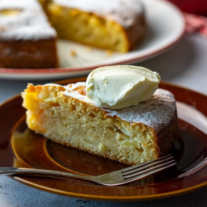 A slice of LIthuanian apple cake with creme fraiche on top on a brown plate.