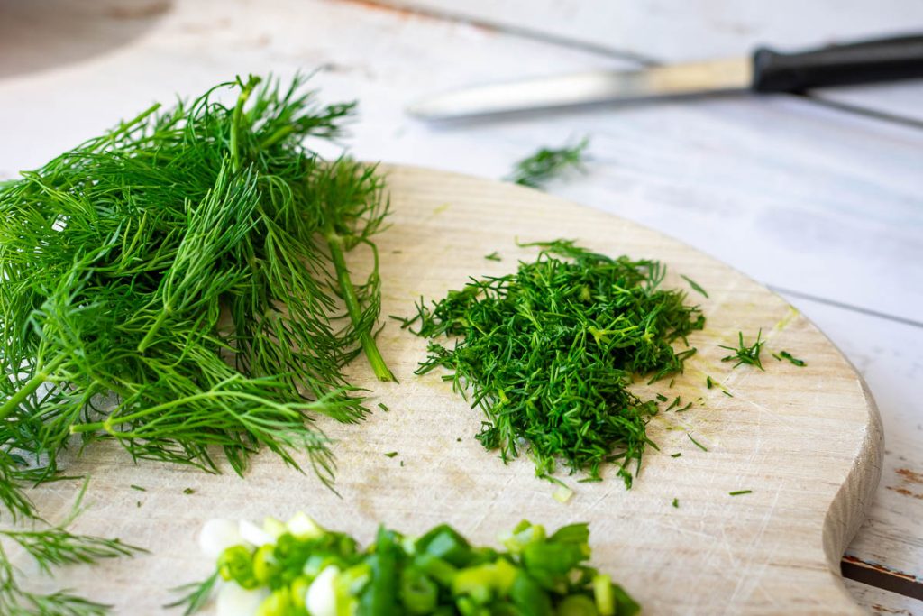 Dill and spring onions on a round wooden board.