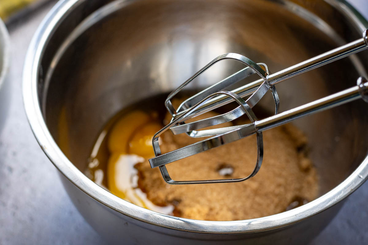 Mixer beaters over eggs and sugar in a metal bowl.