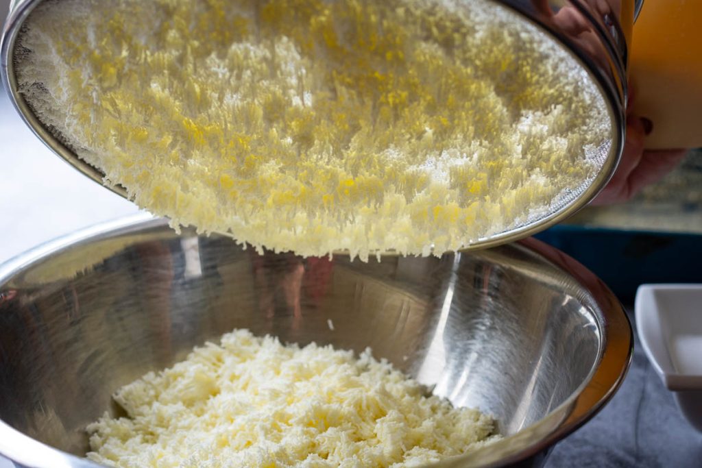 Farmer's cheese pushed trhough the sieve into a metal bowl. 