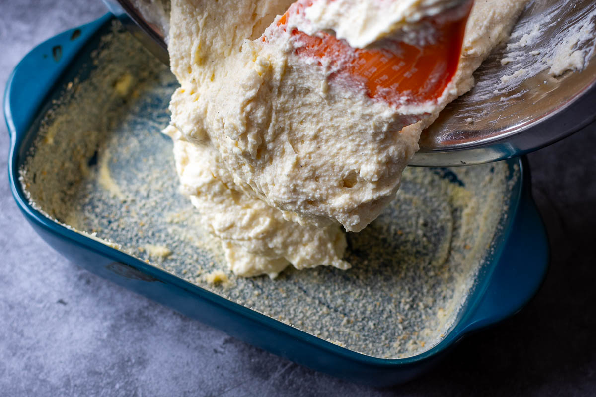 Breakfast cheesecake mixture being scooped into a prepared baking dish. 