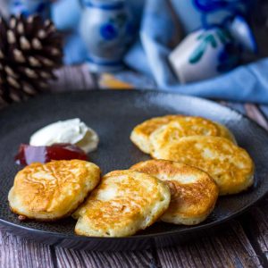 Lithuanian yeasted pancakes with sour cream and jam on a black plate.