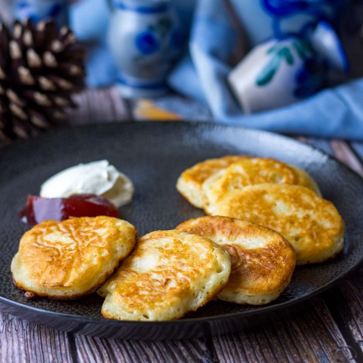 Lithuanian yeasted pancakes with sour cream and jam on a black plate.
