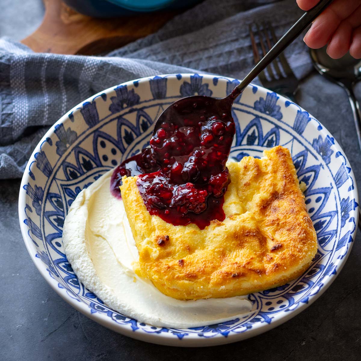 Lithuanian Farmers Cheese Cheesecake in a decirative bowl with sour cream and a spoonful of berry compote.