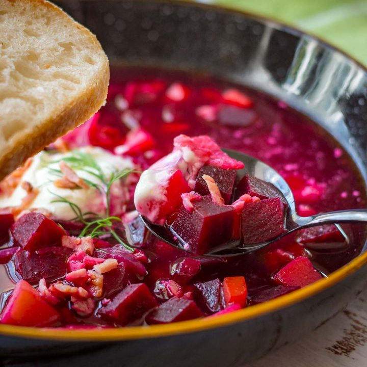 Lithuanian Beetroot Soup with a dollop of sour cream on top and a slice of bread.