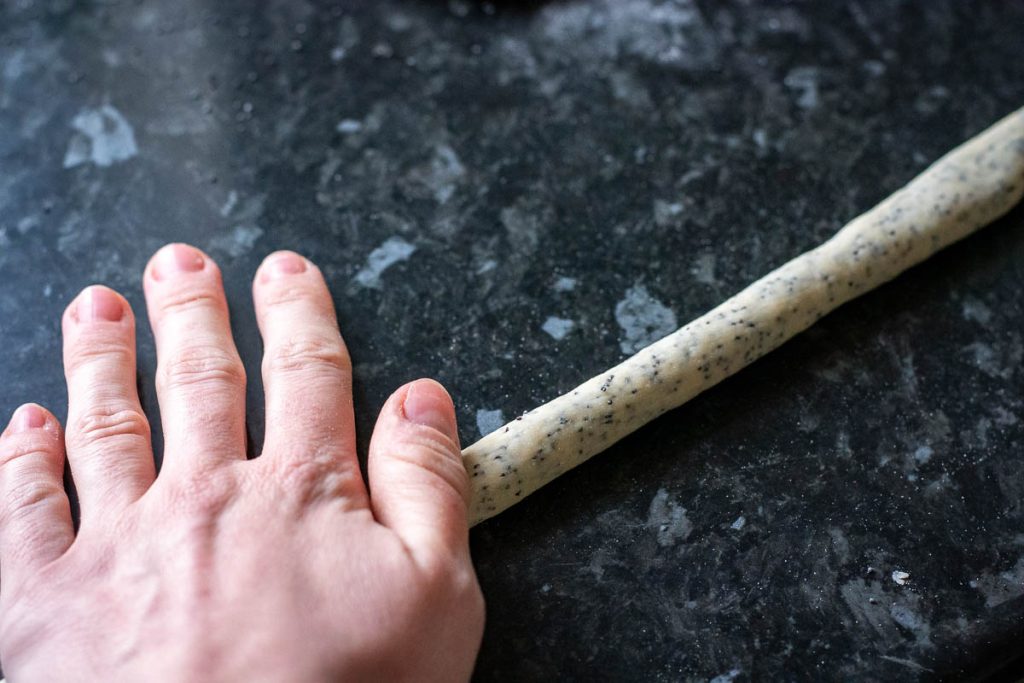 Long strand of poppy seed dough being rolled with palms of hands.