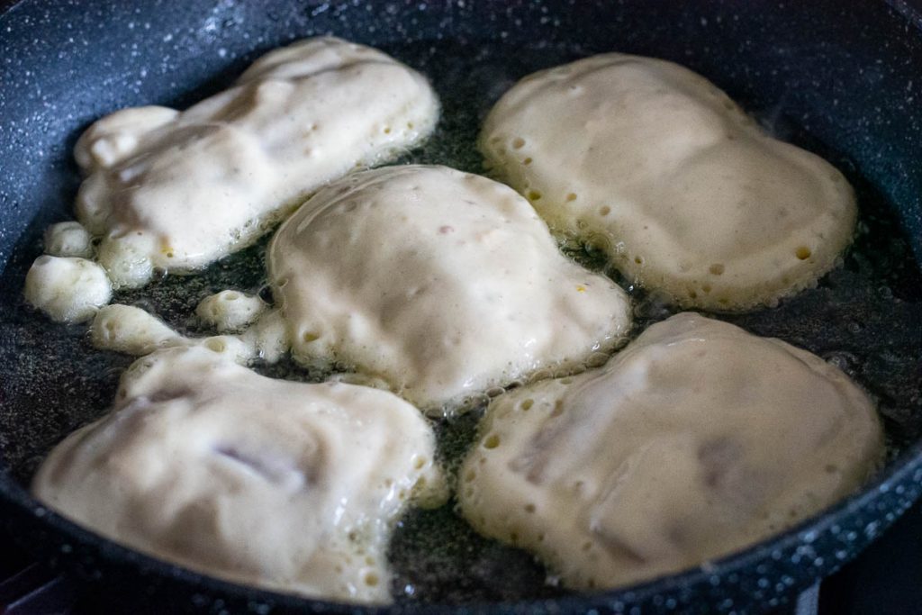 Kefir baterred fish frying in a large frying pan.