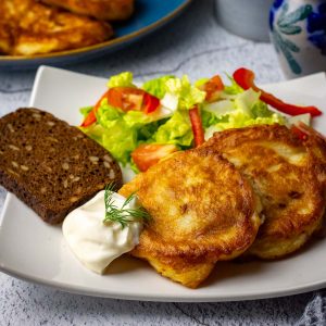 Two pieces of kefir battered pollock on a small white plate with mayo and a side salad.