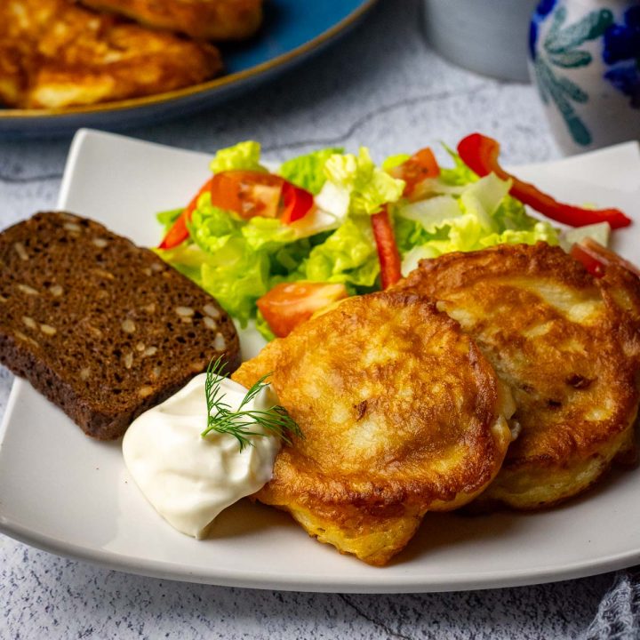 Two pieces of kefir battered pollock on a small white plate with mayo and a side salad.
