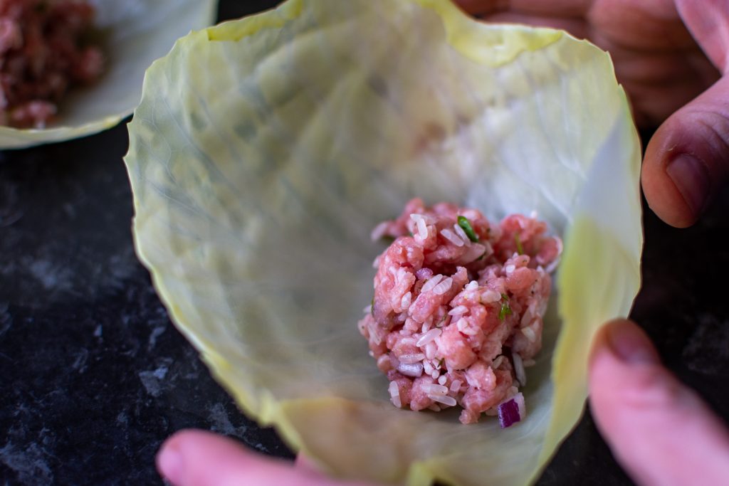 Rolling ground pork filling into a cabbage leaf to make Lithuanian Cabbage Roll. 