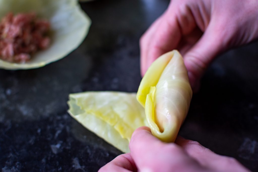Rolling ground pork filling into a cabbage leaf to make Lithuanian Cabbage Roll. 