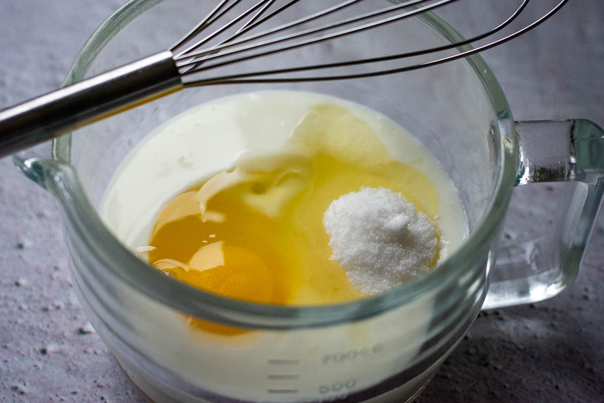 Wet ingredients for Lithuanian pancakes in a glass jug with a balloon whisk resting on the rim. 