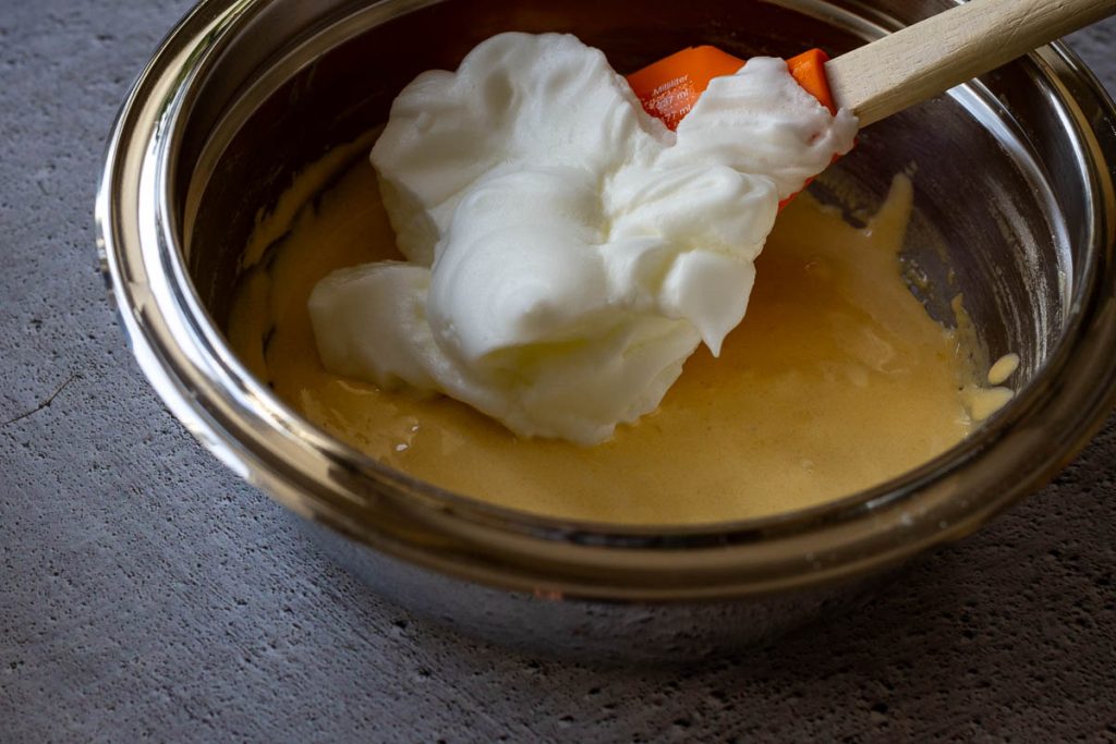 Adding a little of egg whites to the batter with an orange spatula.