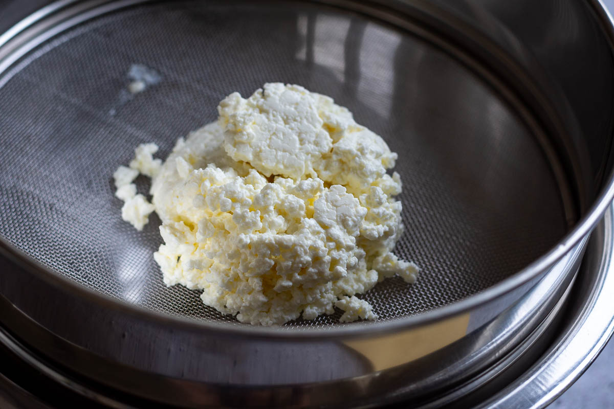 Farmers Cheese on a flat fine sieve over a large mixing bowl.