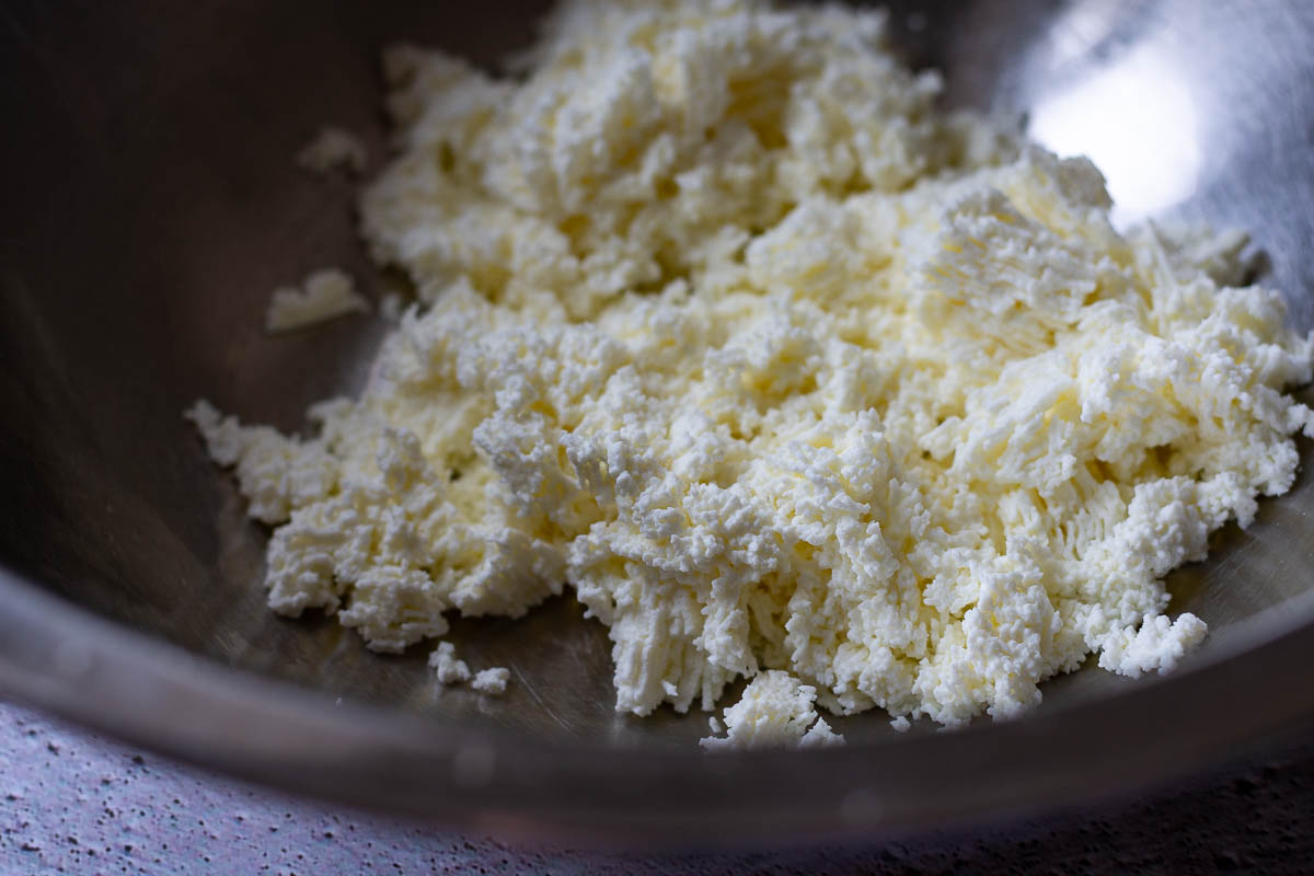 Smoother texture of farmers cheese in a metal bowl after being pushed through a fine sieve.