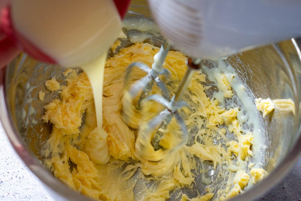 Pouring condensed milk into the beaten butter.