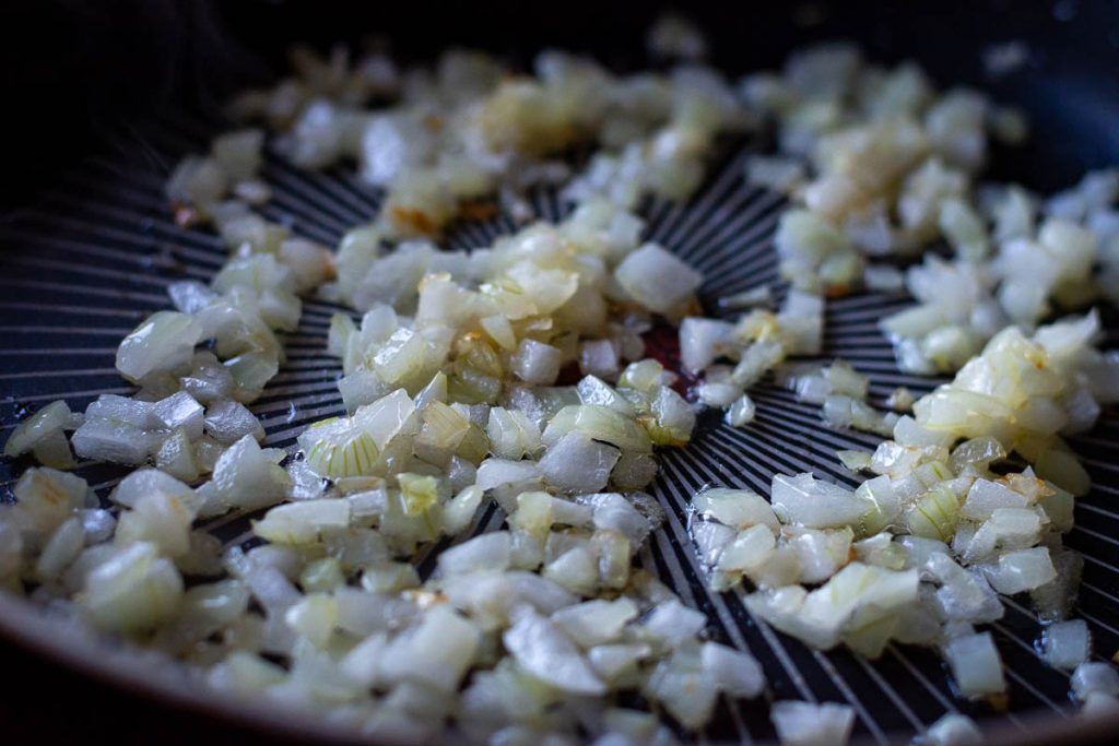 Onions gently sauteing in a frying pan. 