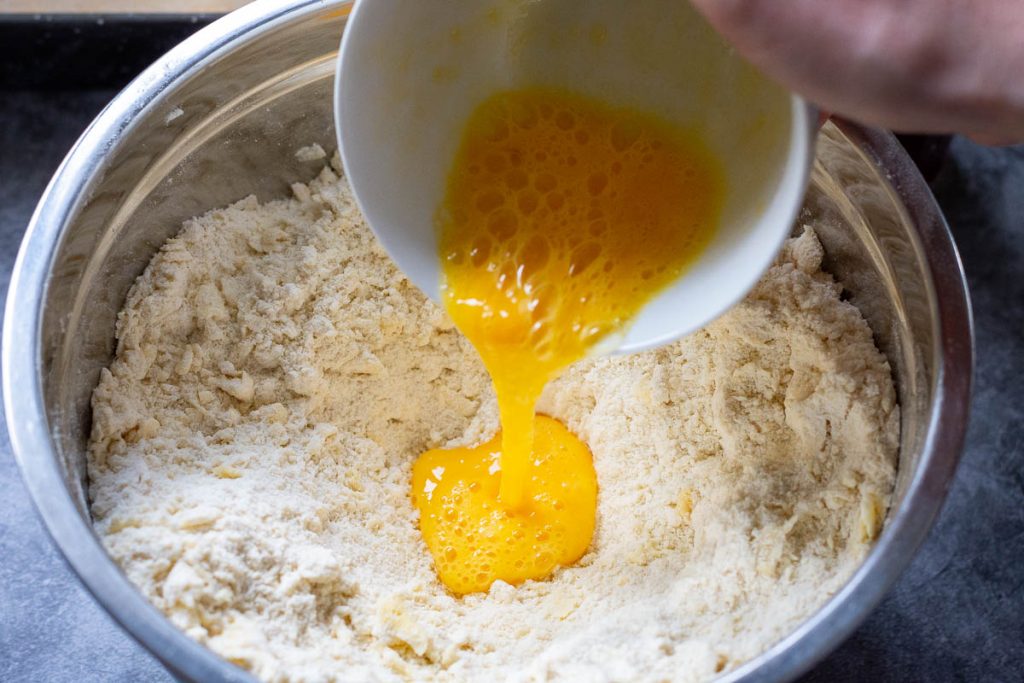 Pouring lightly beaten egg into the crumble mixture. 