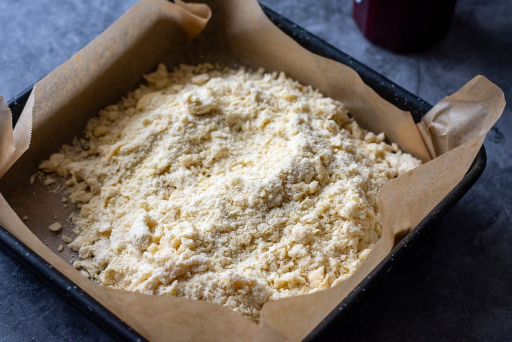 Two thirds of crumble mixture in a square baking tray lined with parchment paper. 