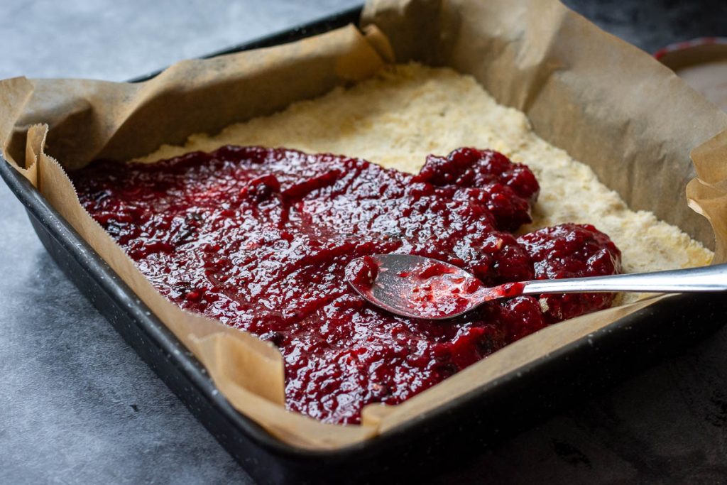 Spreading raspberry jam on top of the buttery pastry base. 