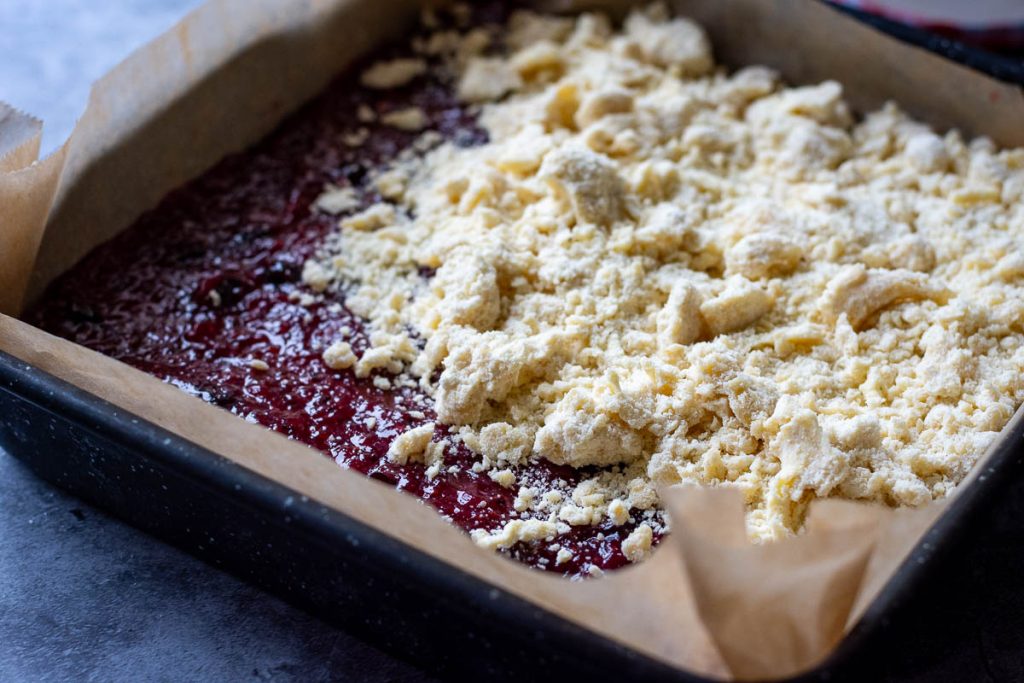 Top layer of the crumble being spread on top of the raspberry jam. 