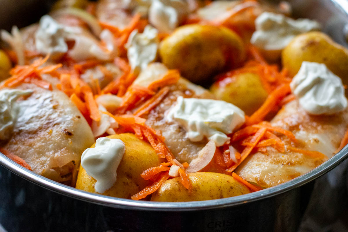 LIthuanian cabbage rolls, potatoes, grated carrots and sliced onion in a large pan with sour cream dollops on top. 