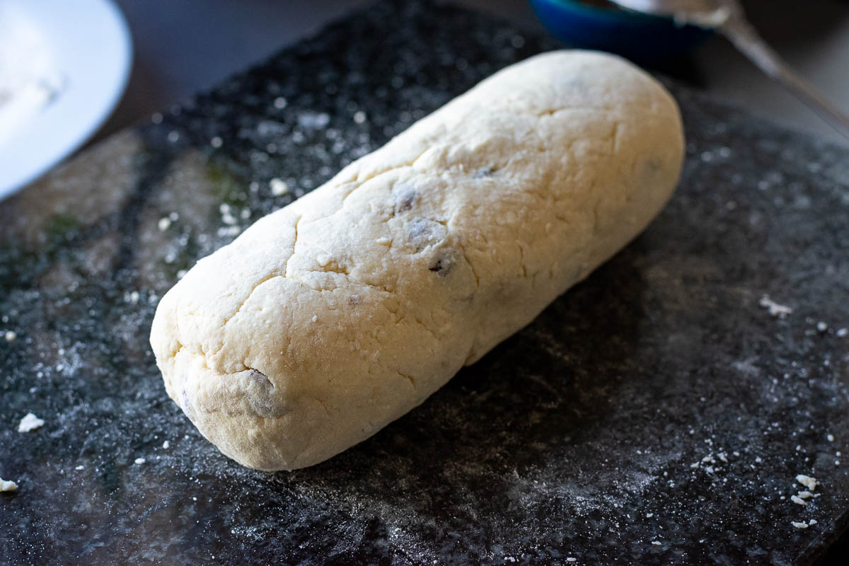 A log of farmers cheese pancake dough on a dark kitchen surface. 