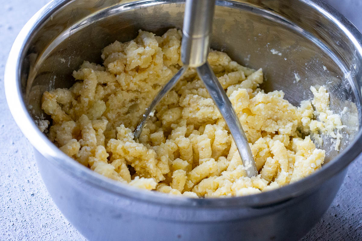 Mashing ingredients into a potato dough using a potato masher.