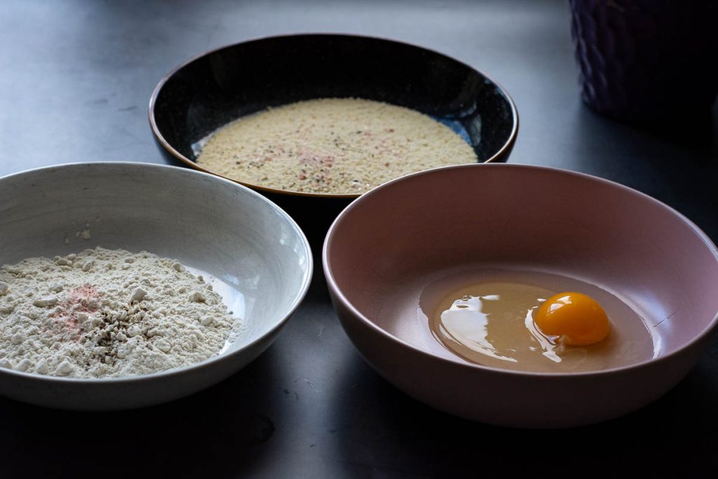 three bowl, one with and egg, another oen with flour, and a third one with breadcrumbs.