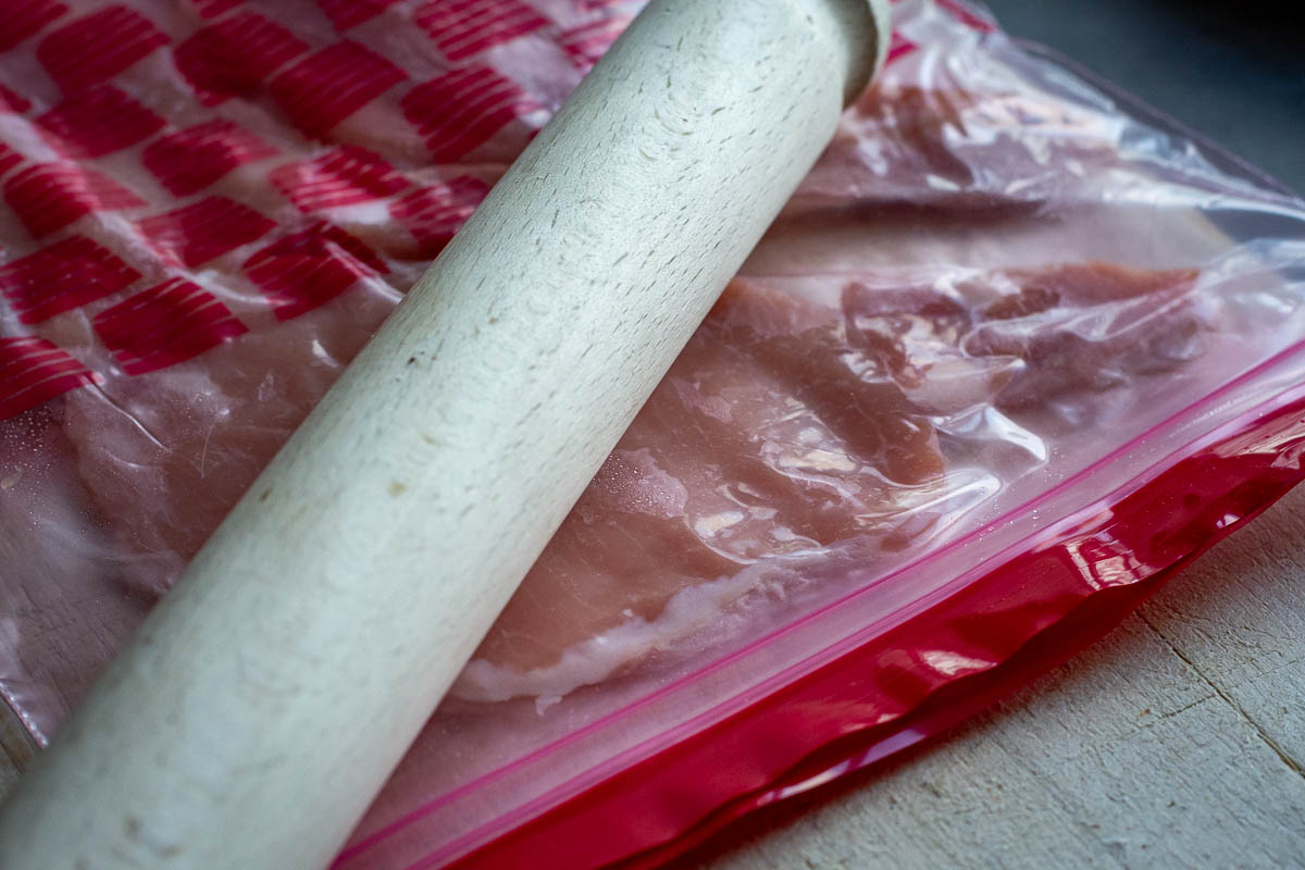 Tendarising pork steaks inside a ziplock bag with a wooden rolling pin.
