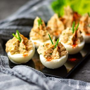 Eight tuna stuffed eggs on a black board garnished with paprika and chives.