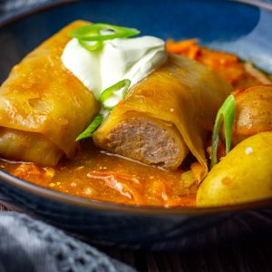 Two LIthuanian Cabbage Rolls in a shallow blue bowl topped with sour cream.