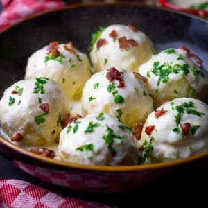 Lithuanian potato dumplings made with boiled potatoes in a black bowl with sour cream sauce and crispy bacon on top.