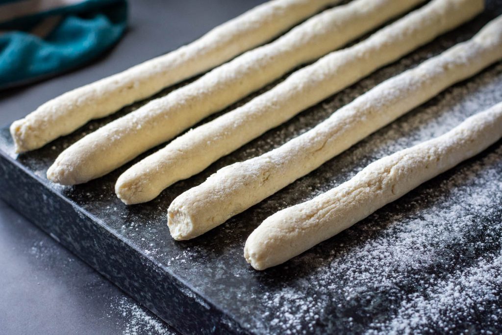 Strings of dough rolled out on a floured surface. 