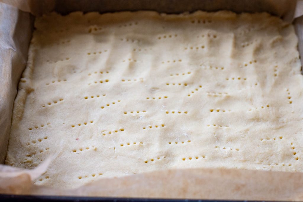 Pastry dressed into the base of a square lined baking pan.