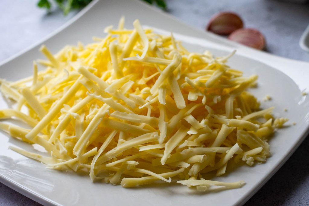 Coarsely grated Cheddar on a white plate.