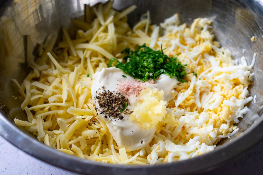 All ingredients for the Lithuanian Eggs and Cheese Salad in a metal bowl unmixed.