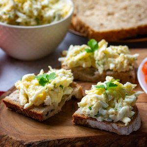 Lithuanian Egg Salad With Cheese on pieces of bread on a woode board.