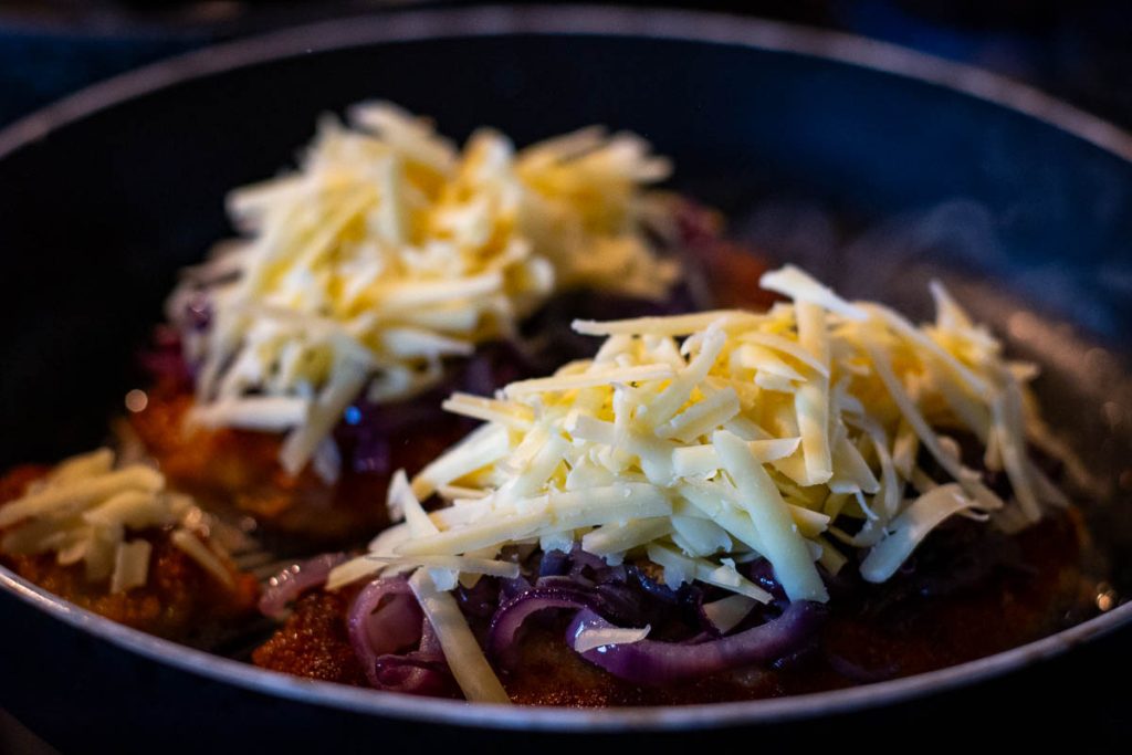 Grated cheese on top of pork cutlets with onions.