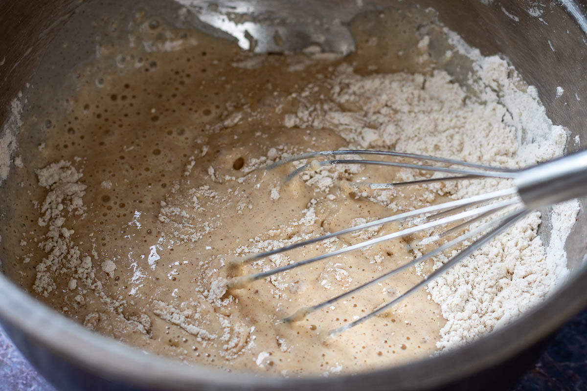 Mixing wet ingredients into the dry ingredients in a large metal bowl. 