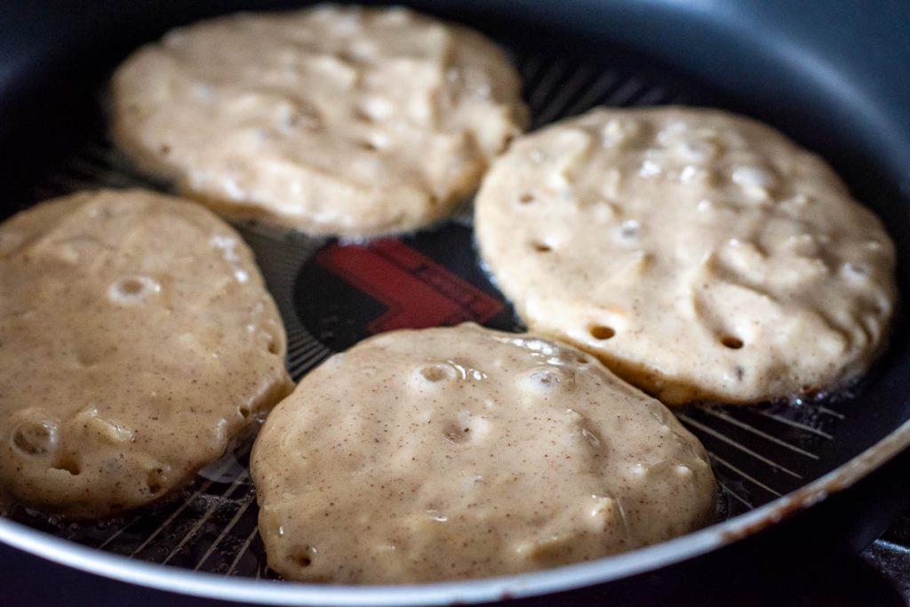 Four grated apple pancakes in a frying pan. 