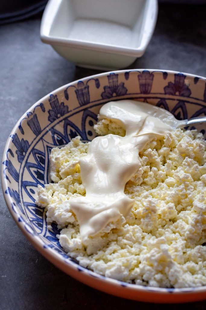 Spooning sour cream on top of farmer's cheese.
