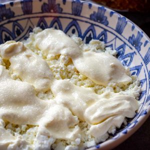 Lithuanian breakfast containing farmer's cheese, sour cream and sugar in a shallow decorative bowl.
