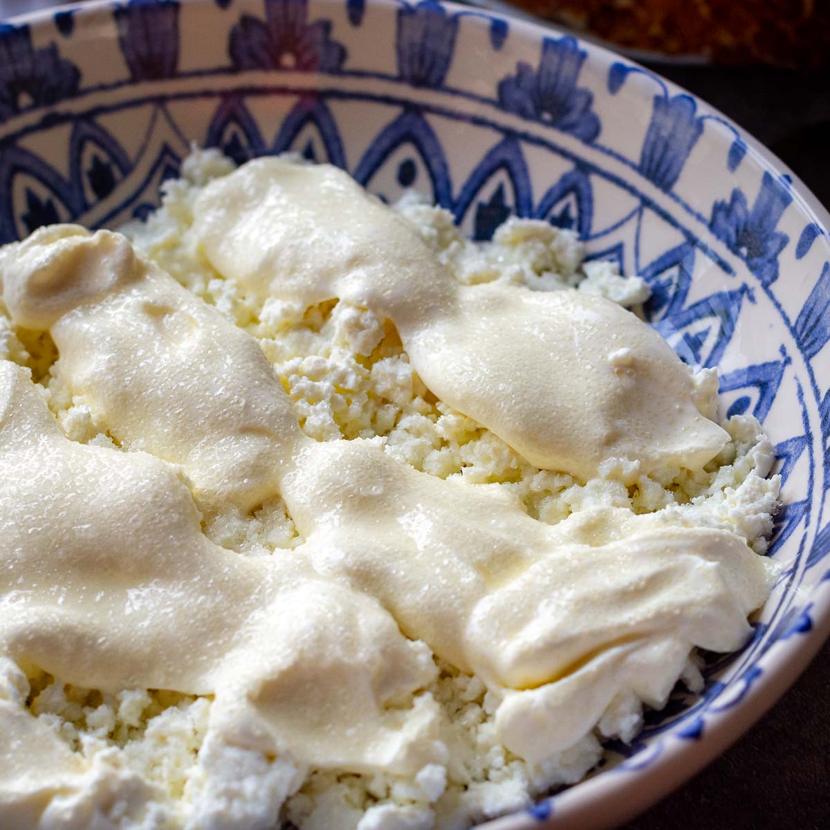 Lithuanian breakfast containing farmer's cheese, sour cream and sugar in a shallow decorative bowl.