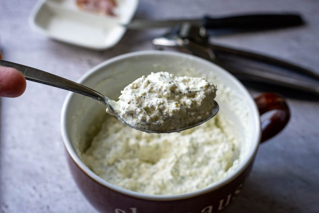 Farmers cheese dip mixed and some is in a spoon hovering above the bowl.