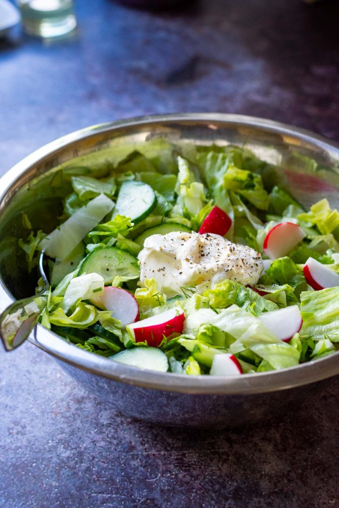 A dollop of sour cream and seasoning on top of the fresh vegetables. 