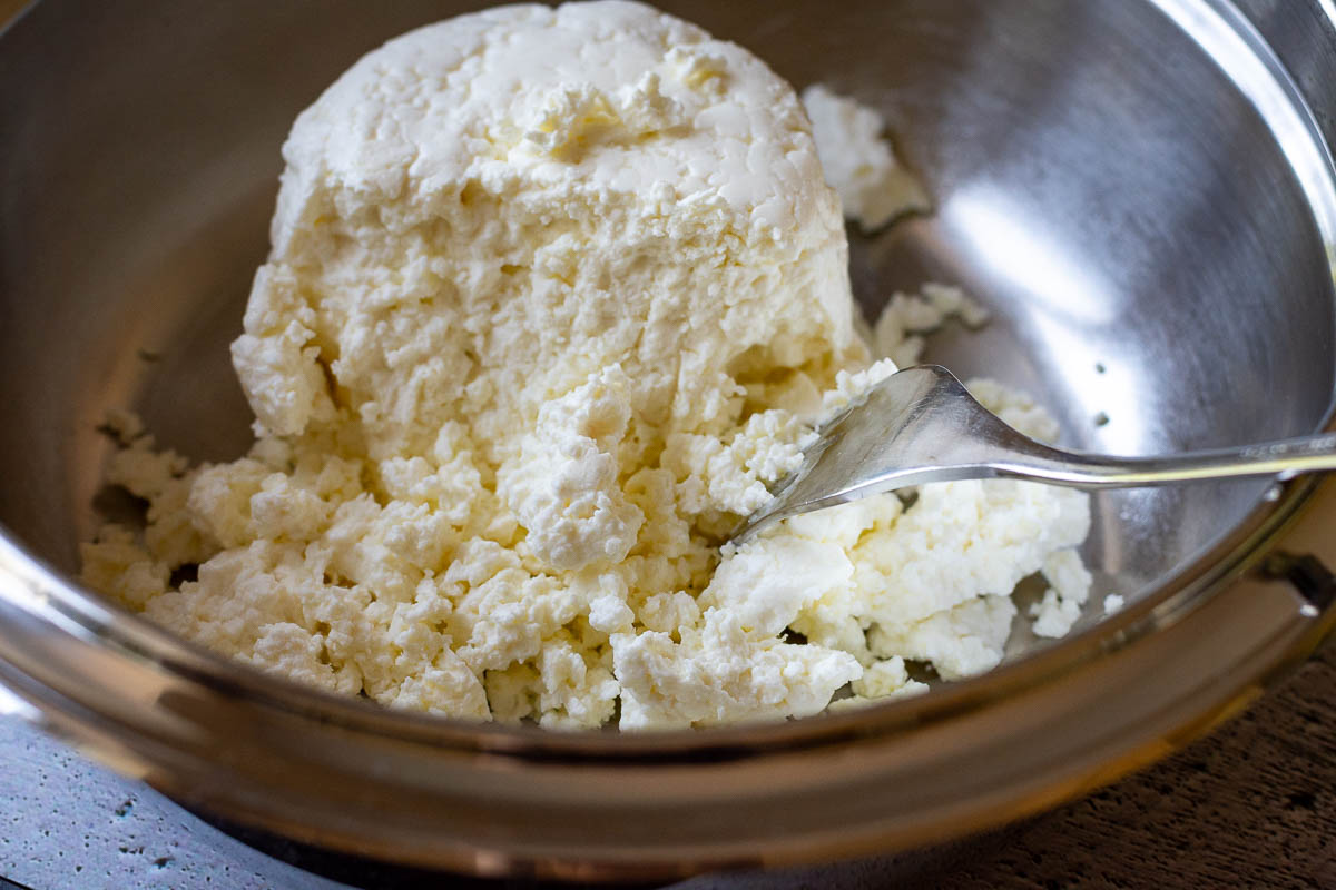 Fluffing up farmer's cheese with a fork in a metal bowl.