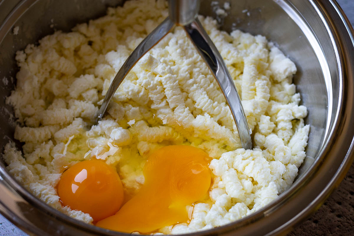 Mashing farmer's cheese, sugar, salt and eggs with a potato masher.