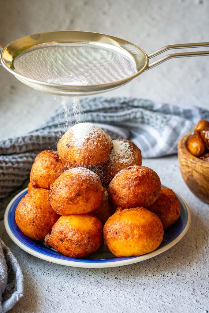 Lithuanian donuts being dusted with powdered sugar.