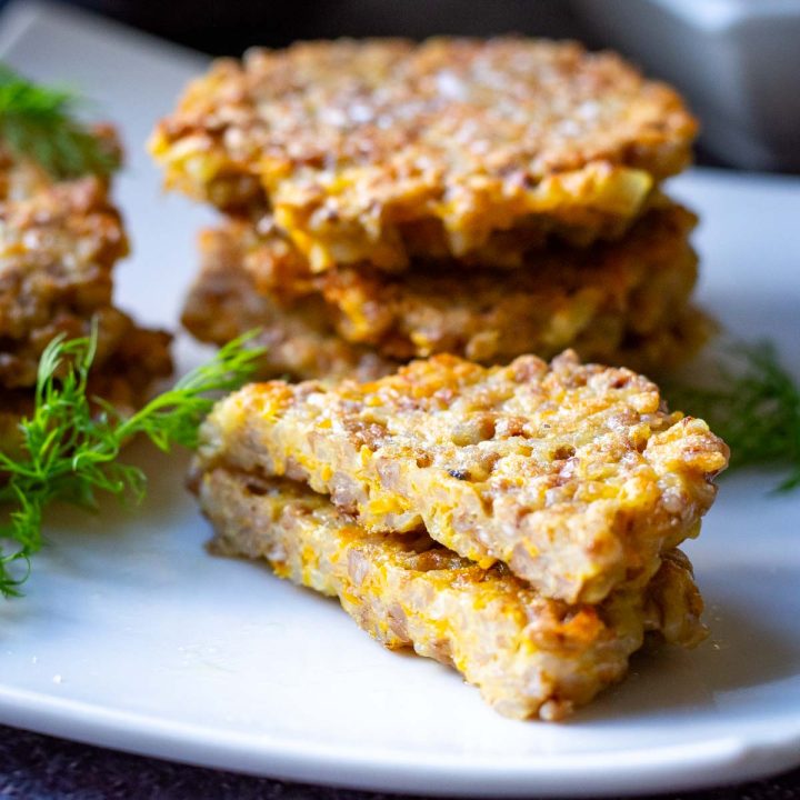 Buckwheat fritters in stacks on a white plate garnihsed with dill.